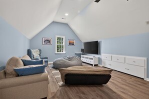 Een moderne loft slaapkamer met een schuine plafond, een bed, een pluchen zitkussen, een televisie en een witte dressoir.