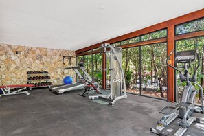 A gym with exercise equipment, a stone wall, and large windows. - Casa Jarrones Tulum- 3-bedroom condo w AC and gym-Pool/Gated/Near Beach/Cenotes (Tulum)