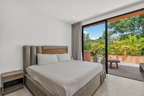 Quarto moderno com cama grande, cabeceira de madeira e vista para um jardim por uma porta de vidro deslizante.