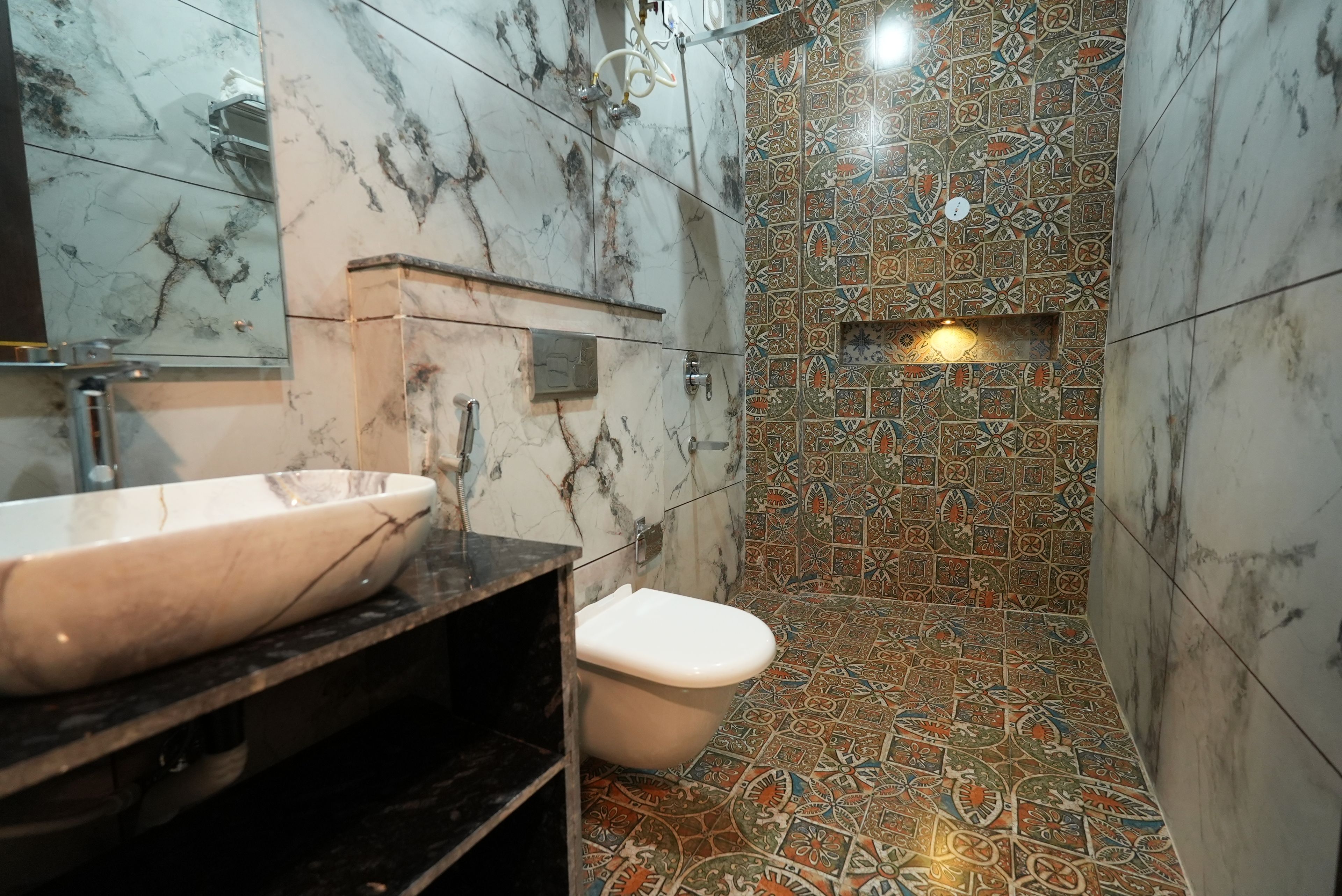 Un baño con lavamanos de mármol, inodoro y zona de ducha con azulejos estampados.