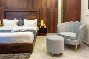 Un dormitorio con cama, mesitas de noche, lámpara, silla y reposapiés.