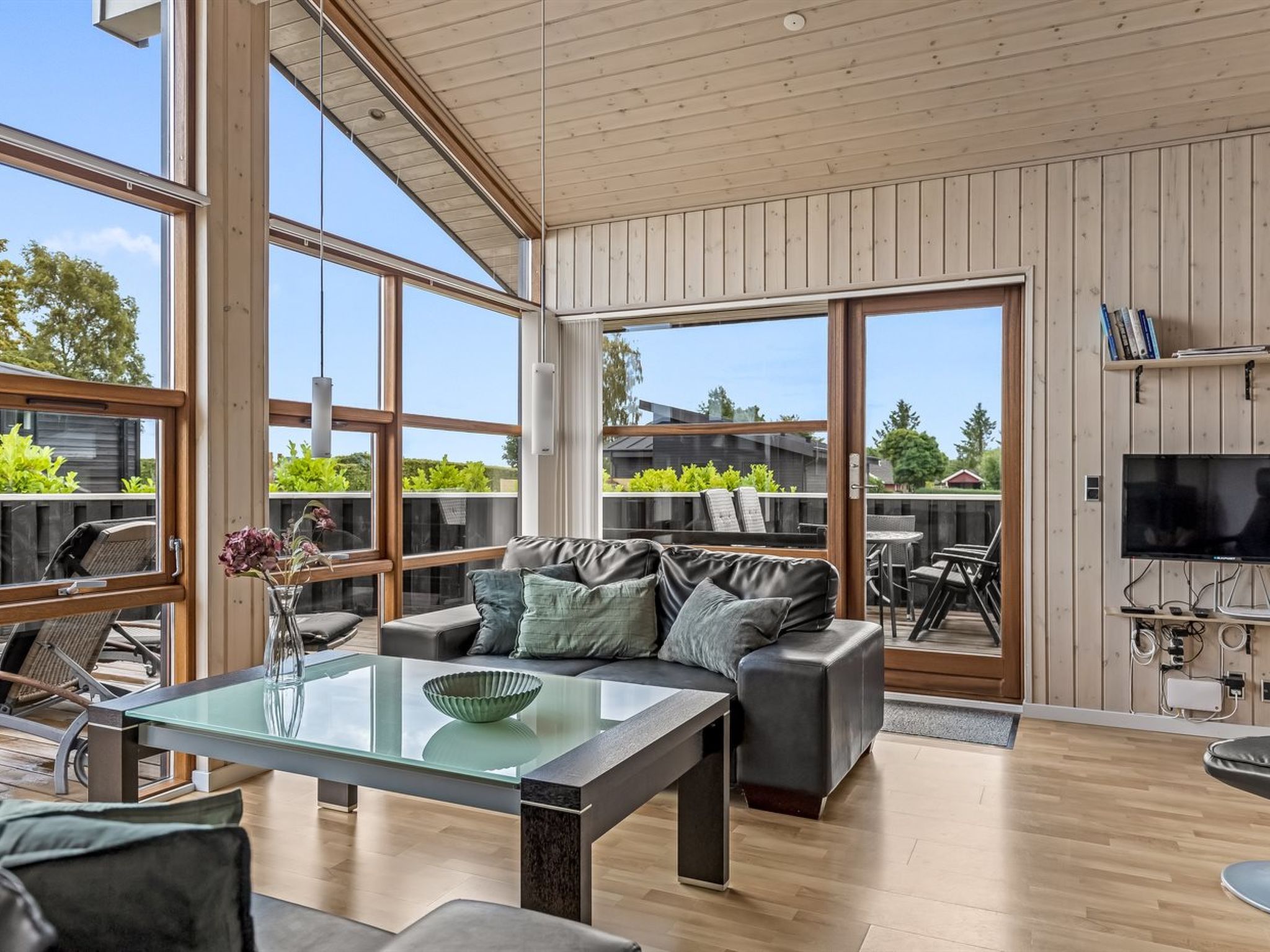 A modern living room with a glass coffee table, leather sofa, and large windows.