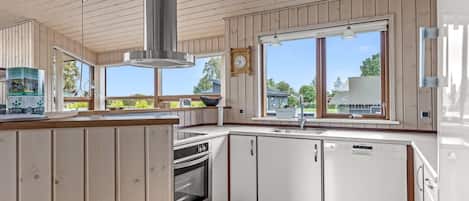 A modern kitchen with wooden paneling, a stainless steel range hood, a dishwasher, and a large window offering a view of the outdoors.