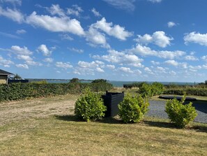 A grassy outdoor area with a clear sky, a body of water in the distance, and a building on the left. - "Thrine" - 150m from the sea by Interhome (Sjølund)