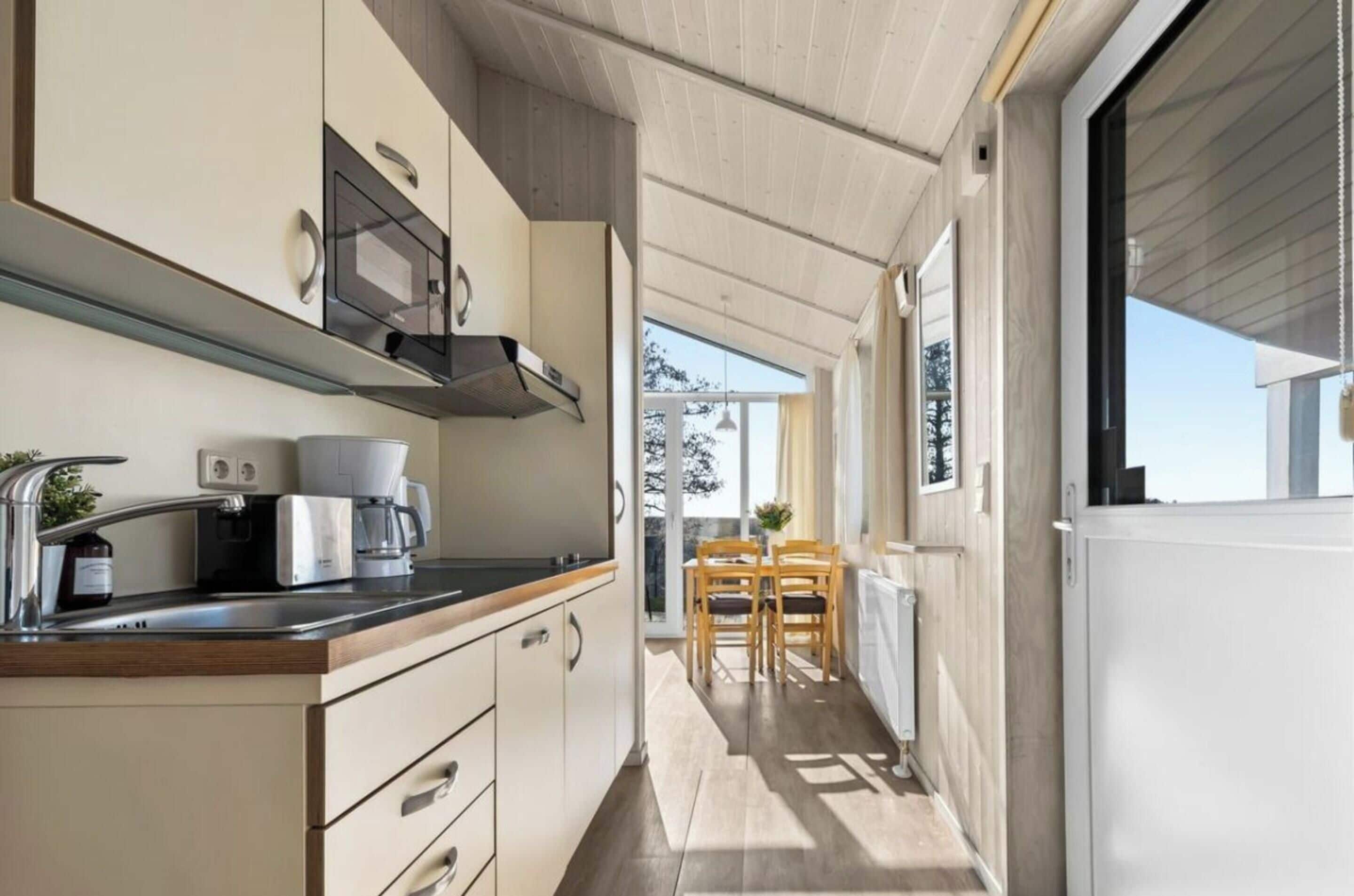 Een kleine keuken met een koffiezetapparaat, een magnetron en een kookplaat. Er is een eethoek met een tafel en stoelen.