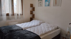 A bedroom with two beds, a wooden shelf unit, a window with sheer curtains, and wall art. - Apartment in Orelle Near Ski Lift (Orelle)