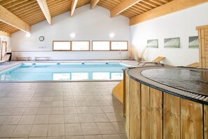 An indoor swimming pool with wooden beams, tiled floor, and a hot tub area. - Apartment in Orelle Near Ski Lift (Orelle)