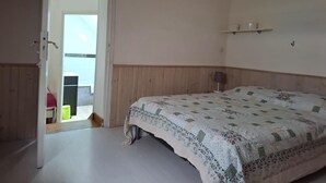 A bedroom with a bed, a door leading to an outdoor area, and a small shelf with items on the wall. - Charming Normandy Escape for Three (Courtils)