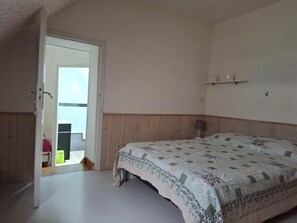 A bedroom with a bed, a door leading to an outdoor area, and a small shelf with items on the wall. - Charming Normandy Escape for Three (Courtils)