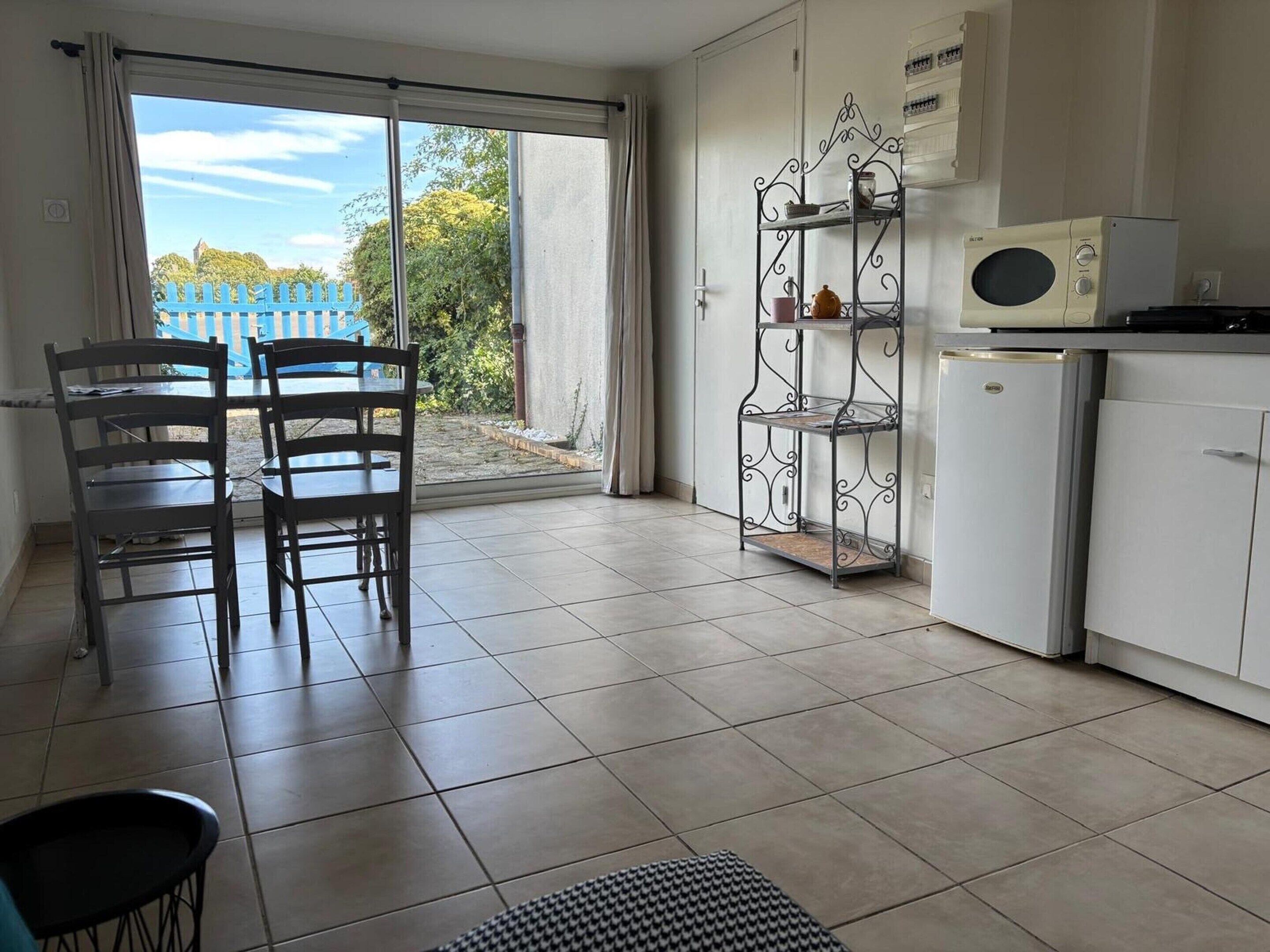 A room with a dining table and chairs, a kitchen area with a refrigerator, and a sliding glass door leading to an outdoor area.