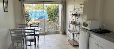 A kitchen with a dining area, a sliding glass door leading to a garden, and a metal rack with kitchen items.