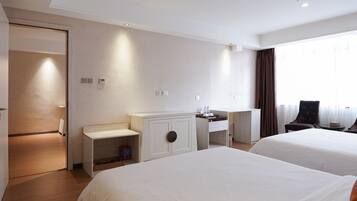 Habitación de hotel con dos camas, un escritorio, una silla y una ventana con cortinas.