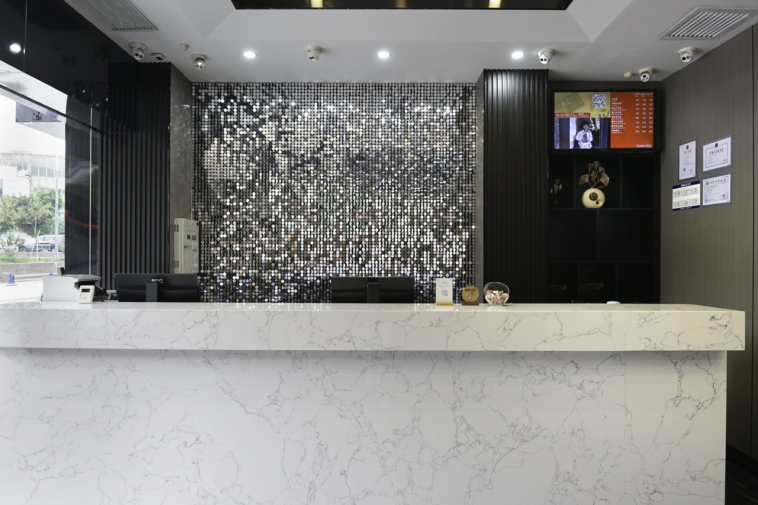 Una recepción con encimera de mármol, una pared decorativa con diseños circulares y una pantalla digital que muestra información.