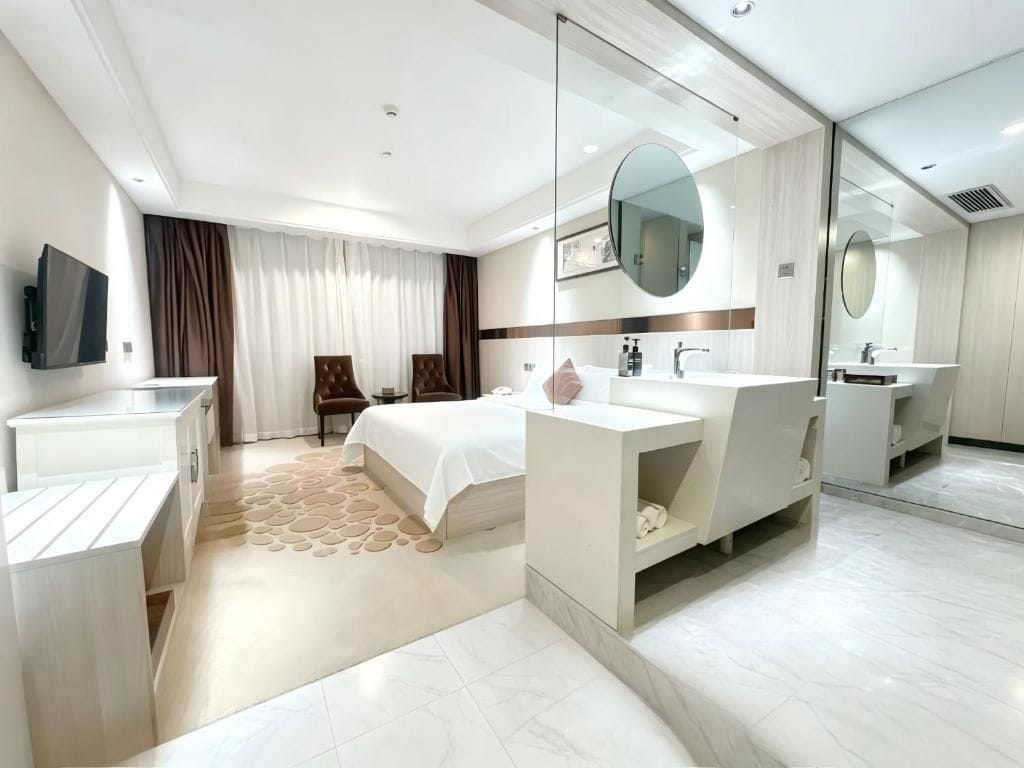 Habitación de hotel moderna con cama, dos lavamanos, televisor de pantalla plana y un espejo grande.