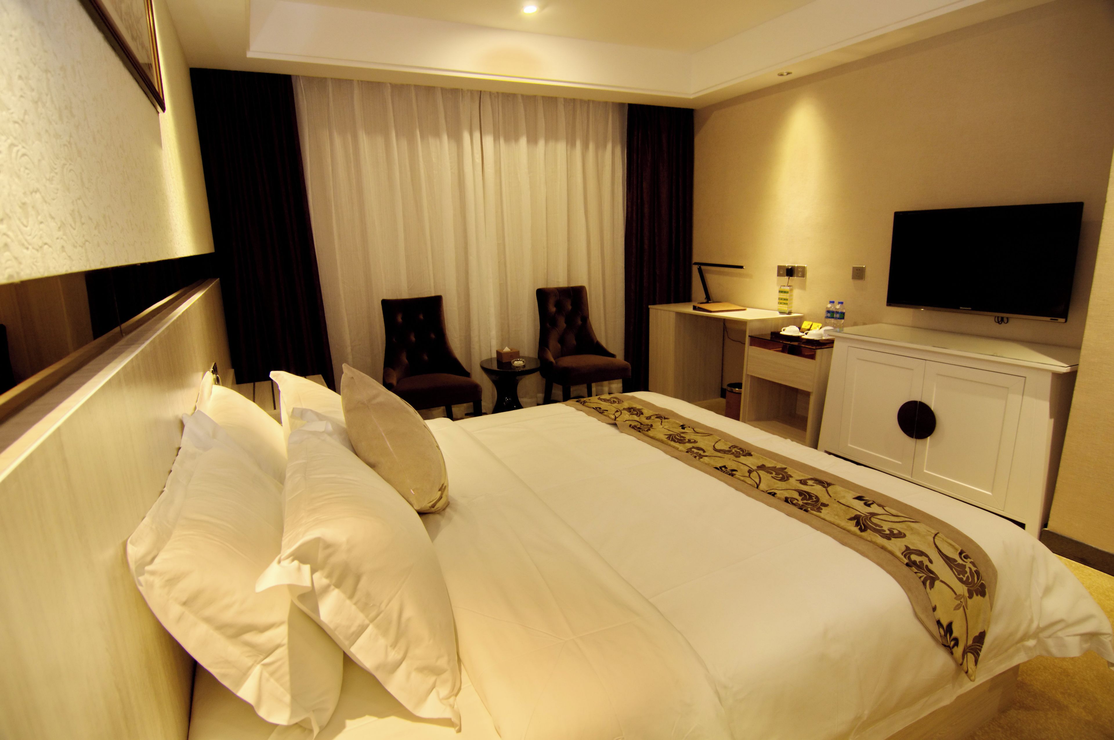 Quarto de hotel com cama, duas cadeiras, escrivaninha, televisão e minibar.