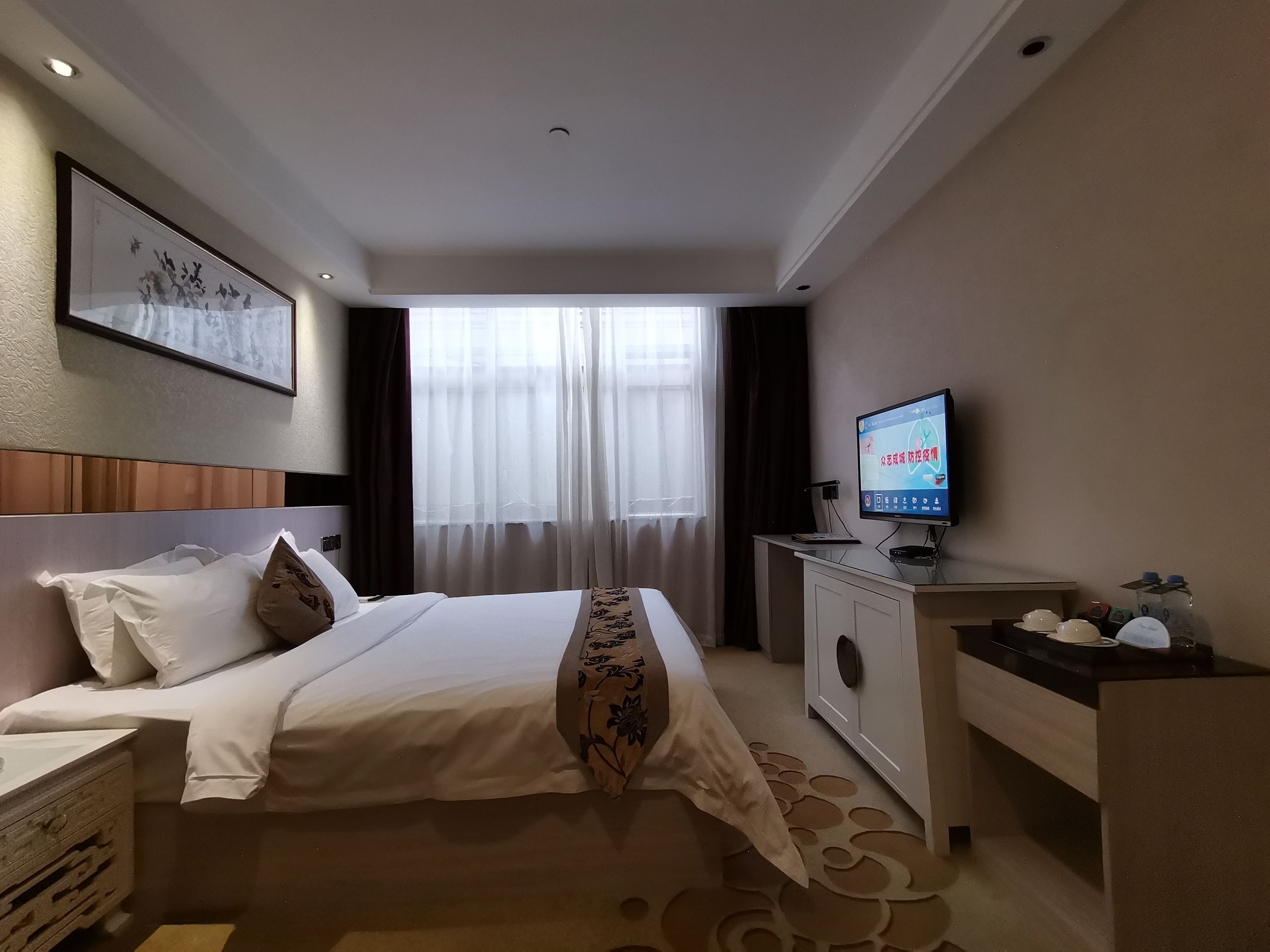 A hotel room with a bed, a television, a desk, and a window with curtains.