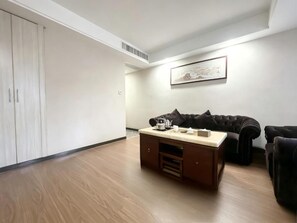 Una habitación con piso de madera, un sofá marrón oscuro, una mesita con una tetera, tazas y una caja, y un cuadro en la pared.