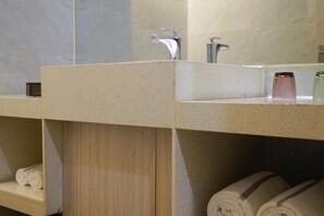 Un baño con encimera color beige, dos lavamanos y un espejo. Hay toallas y un dispensador de jabón en la encimera.