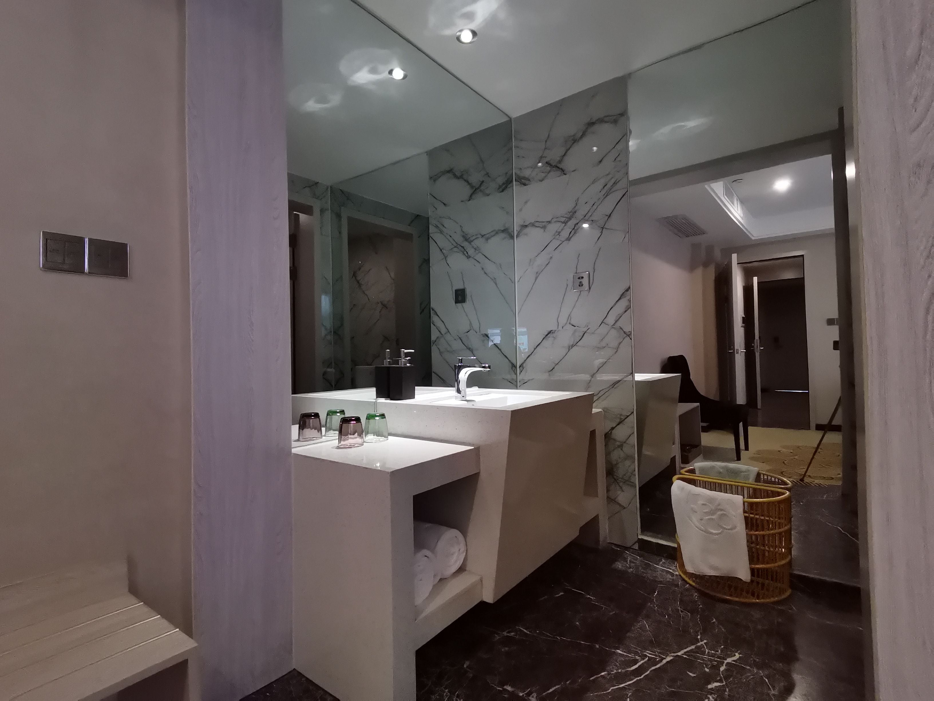 Une salle de bain moderne avec un pare-baignoire en marbre, un lavabo blanc et un miroir.