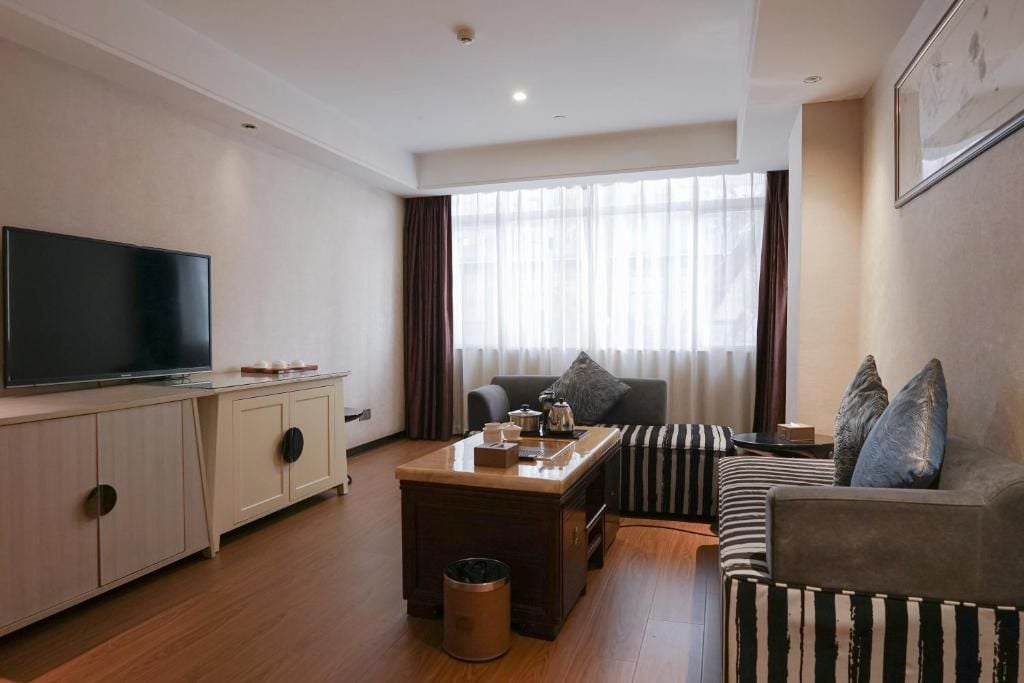 A modern living room with a flat-screen TV, a sofa, a coffee table, and a large window with curtains.