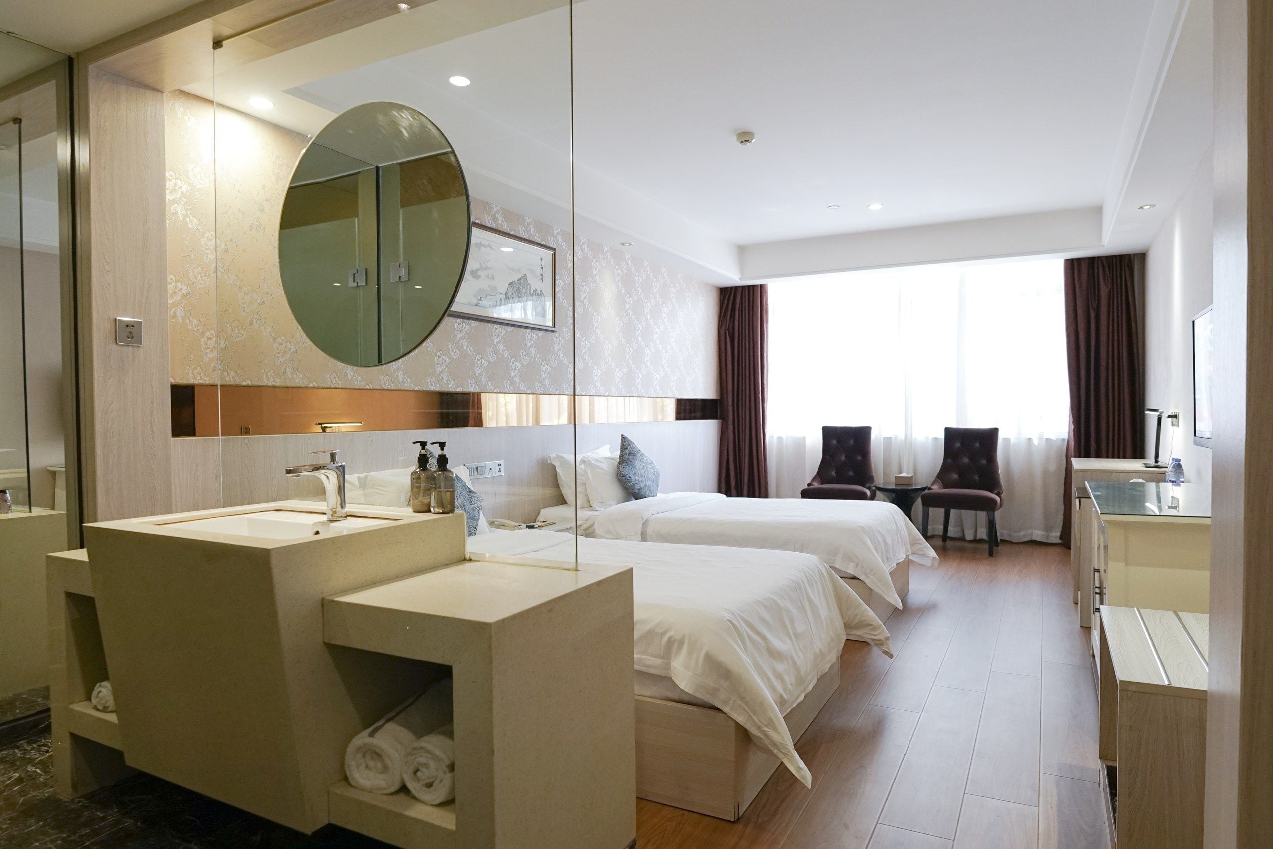 Une chambre d’hôtel avec un grand miroir, deux lits, un bureau et une salle de bain équipée d’un lavabo et d’un espace pour ranger les serviettes.