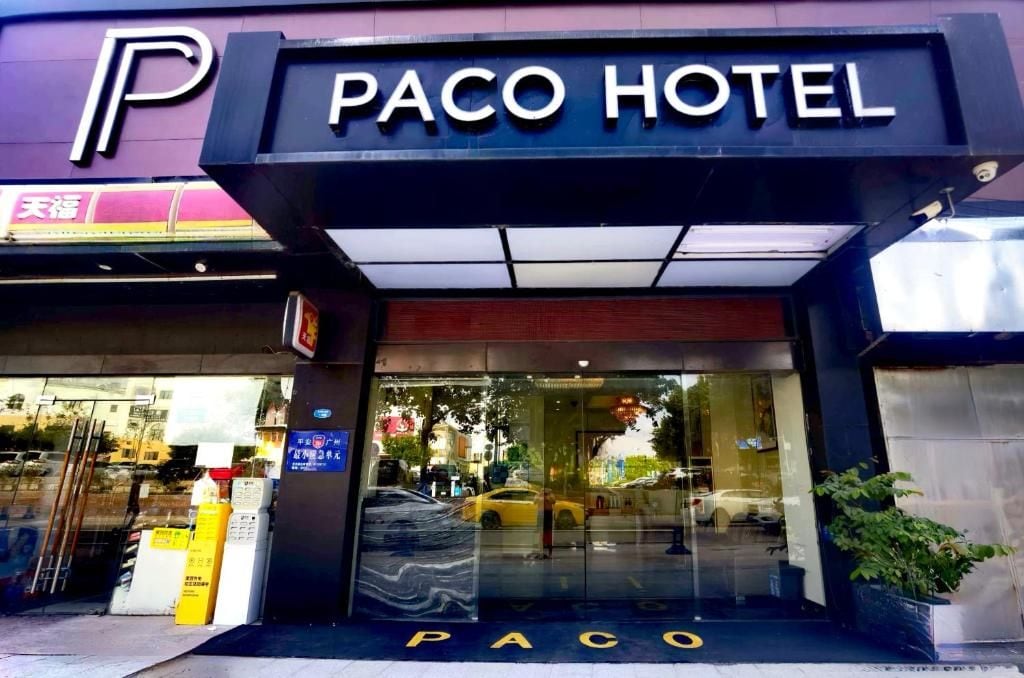 La entrada del Hotel Paco, con fachada de vidrio y un estacionamiento visible al exterior.