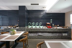 A modern restaurant with a dark tiled backsplash, a counter with kitchen appliances, and seating area with tables and chairs.