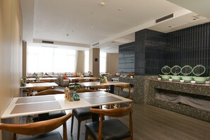 A modern restaurant with multiple dining tables and chairs, a kitchen area with a marble countertop, and a large window providing natural light. - Paco Hotel (Guangzhou Tianhe Coach Terminal Metro Station) (Guangzhou)