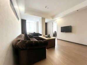 Una sala moderna con un sofá de cuero, un televisor de pantalla plana montado en la pared y piso de madera.