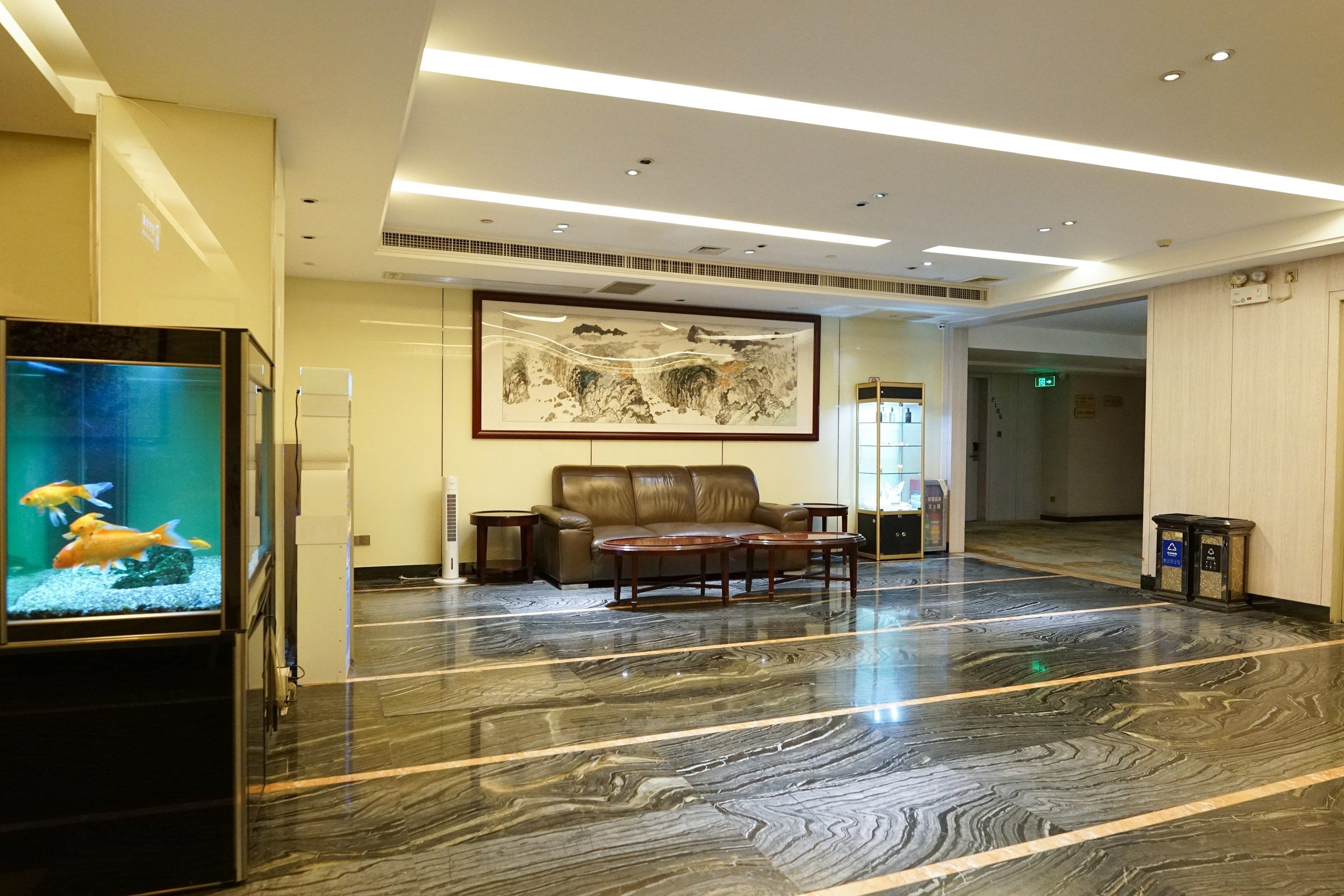 A lobby with a marble floor, a brown leather sofa, a framed artwork, and a fish tank.
