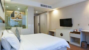 Una habitación de hotel con una cama, televisión, un escritorio pequeño y un espejo.