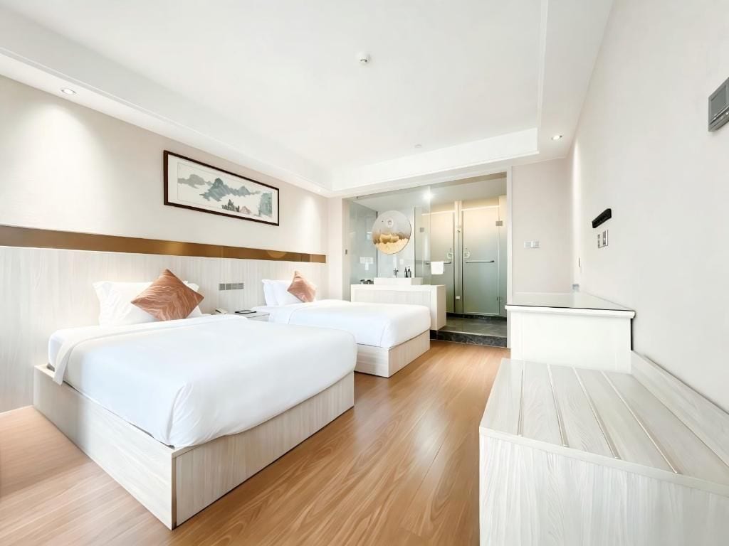 Habitació d'hotel amb dos llits, un escriptori i un bany visible a través d'una porta de vidre.
