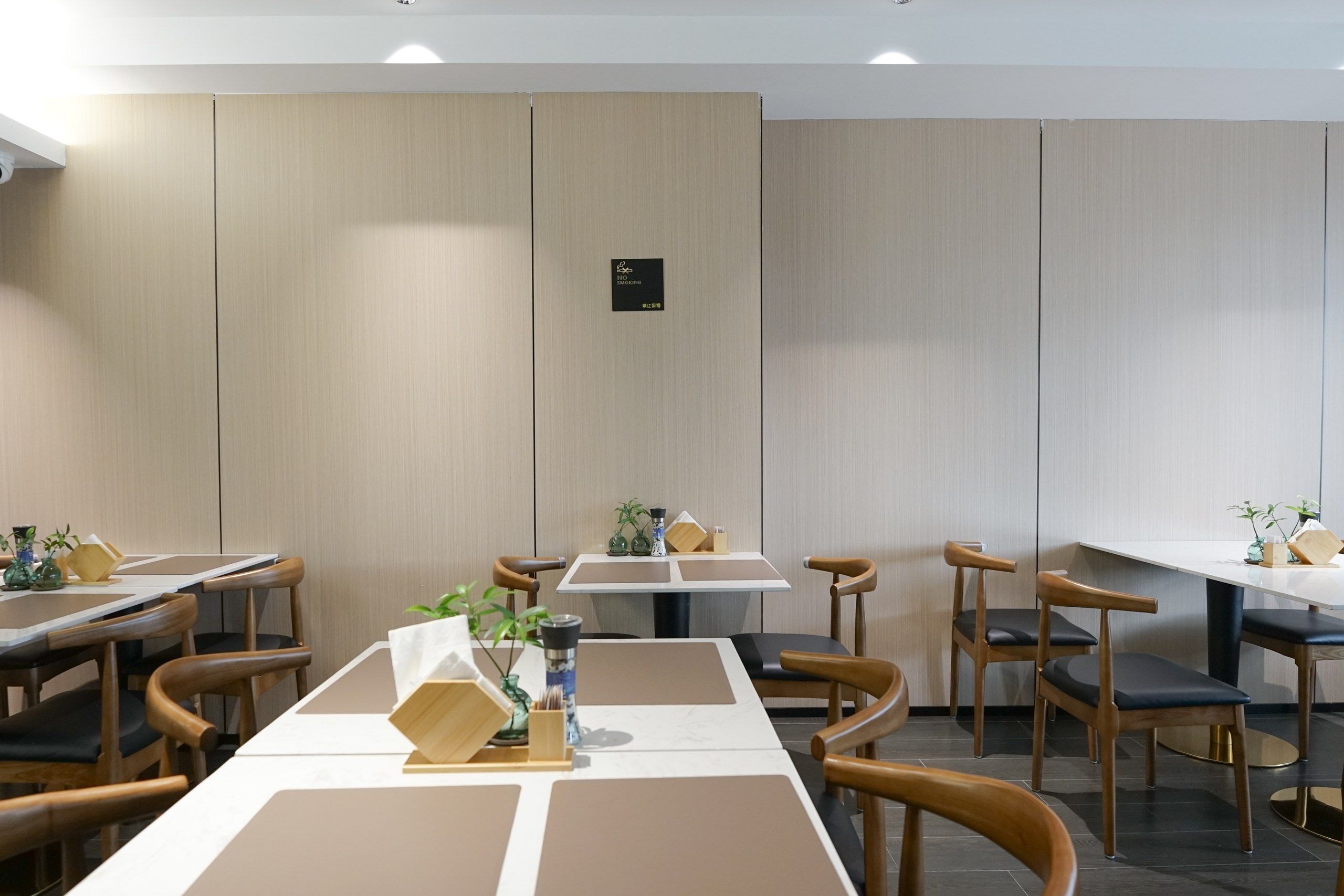 A modern dining area with multiple tables and chairs, a no-smoking sign, and a clean, minimalist design.
