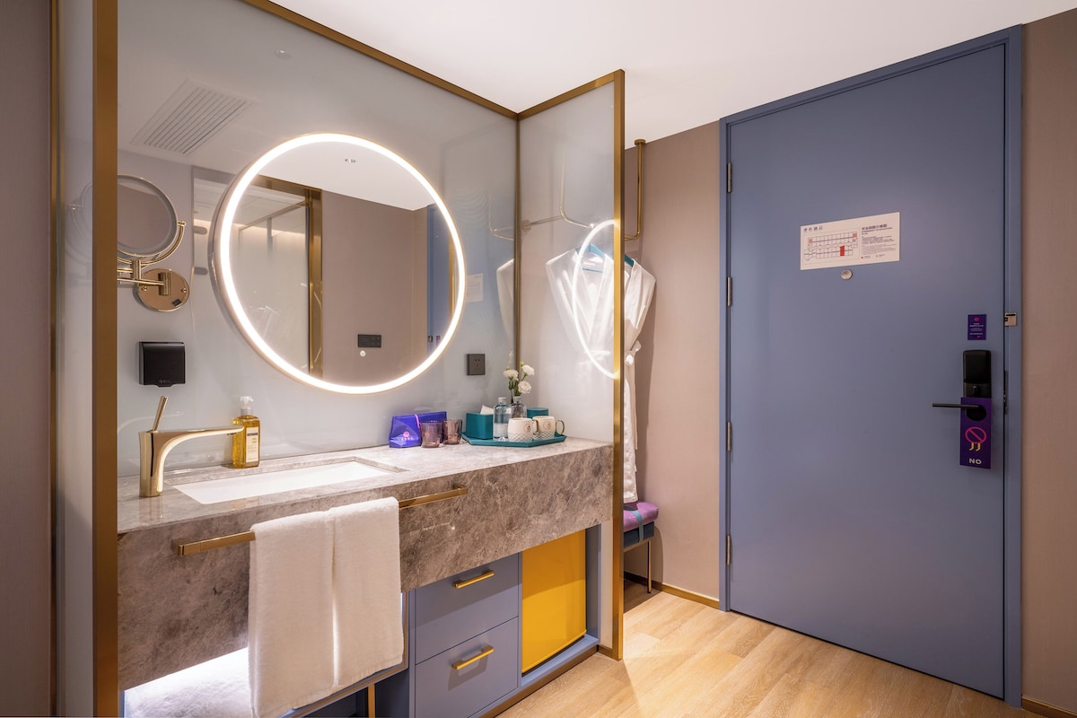 A modern bathroom with a round mirror, vanity, and a blue door with a security lock.
