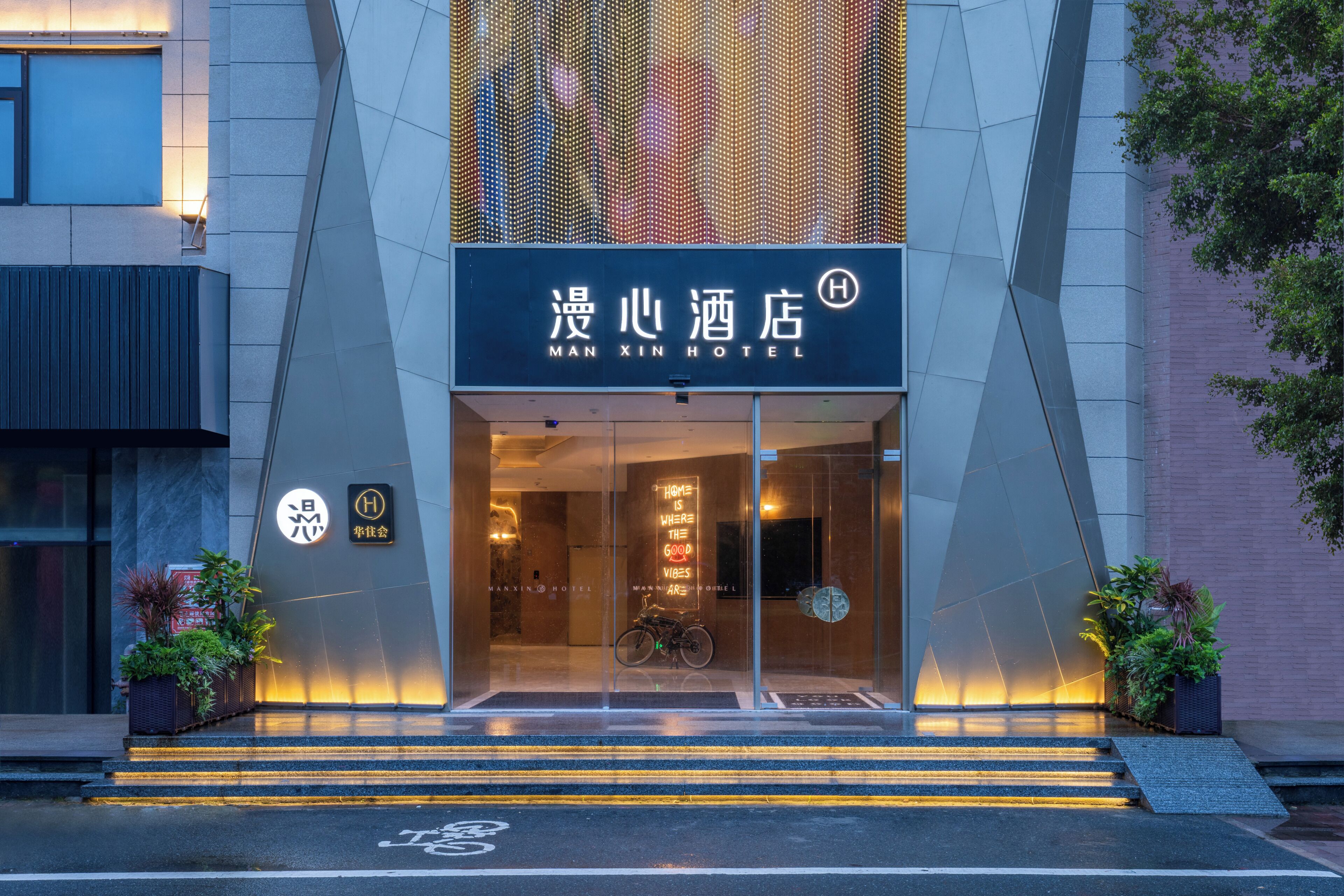 A hotel entrance with a modern design, featuring a large glass facade, a bicycle parked outside, and a staircase leading up to the entrance.