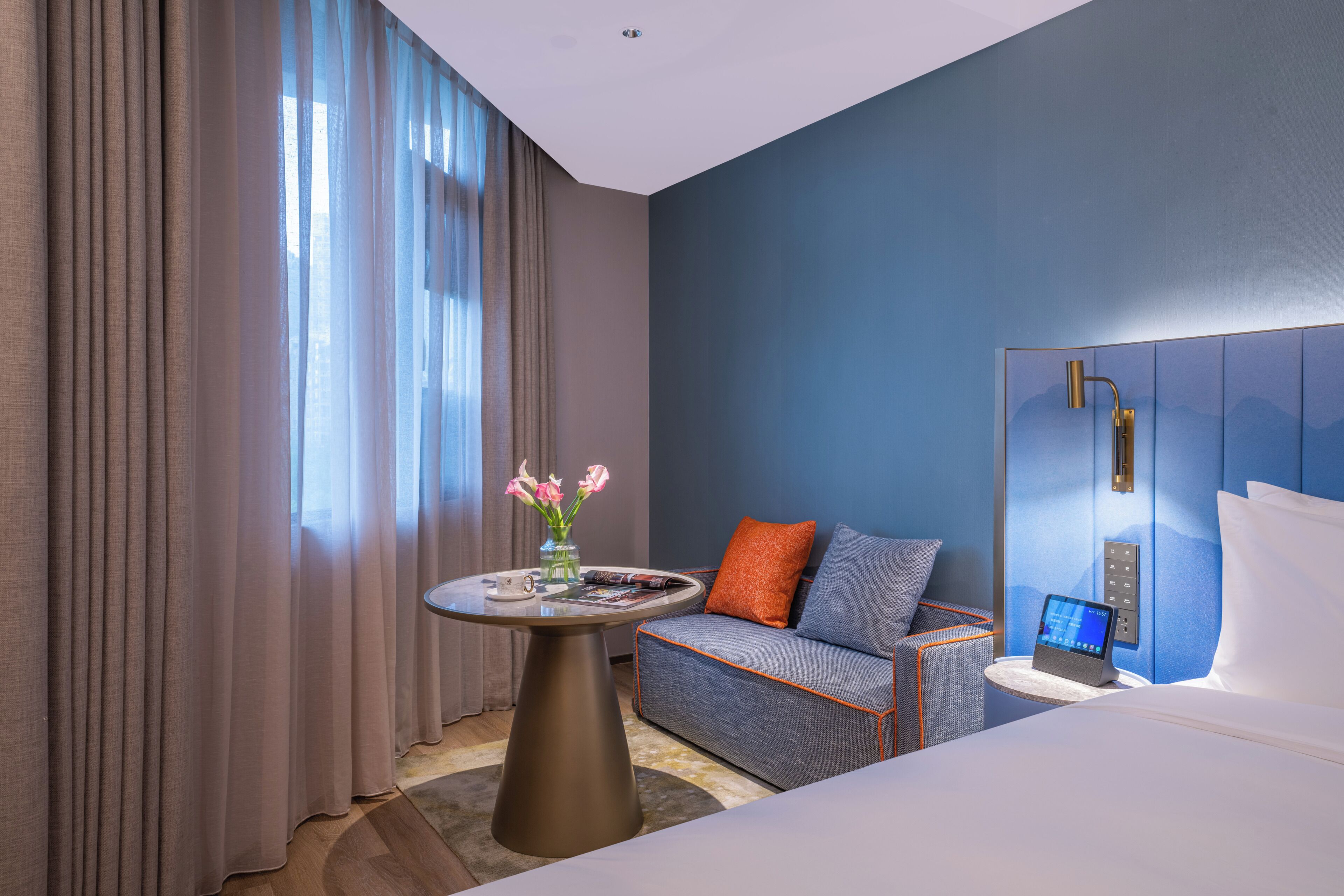 Habitación de hotel con cama, sofá, una mesita con un jarrón de flores y televisión instalada en la pared.