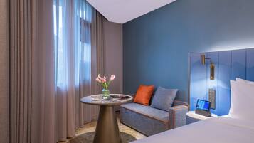 Habitación de hotel con cama, sofá, una mesita con un jarrón de flores y televisión instalada en la pared.