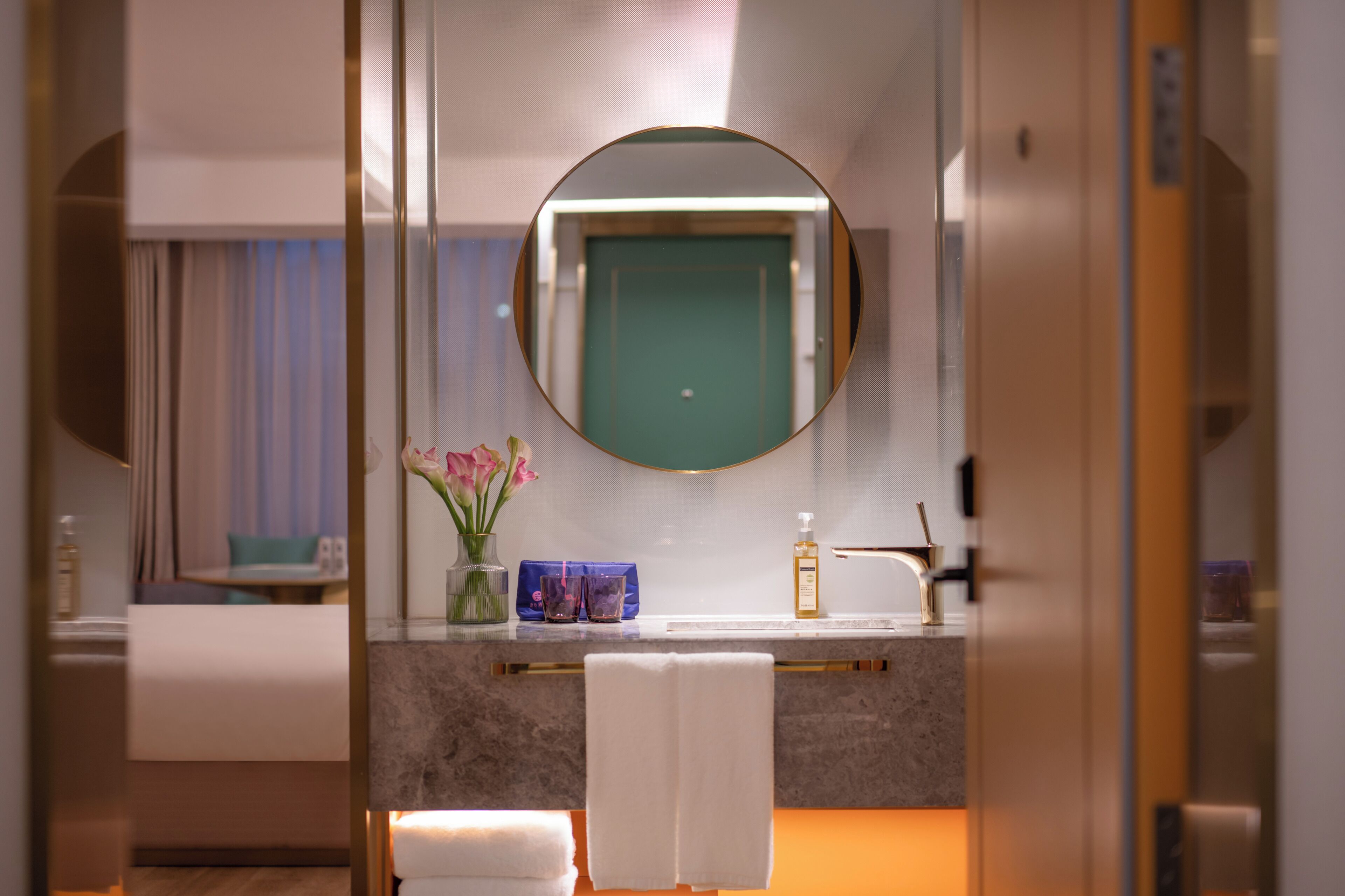 A bathroom with a round mirror, a sink, a towel, and a vase with flowers.
