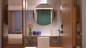 A bathroom with a round mirror, a sink, a towel, and a vase with flowers.