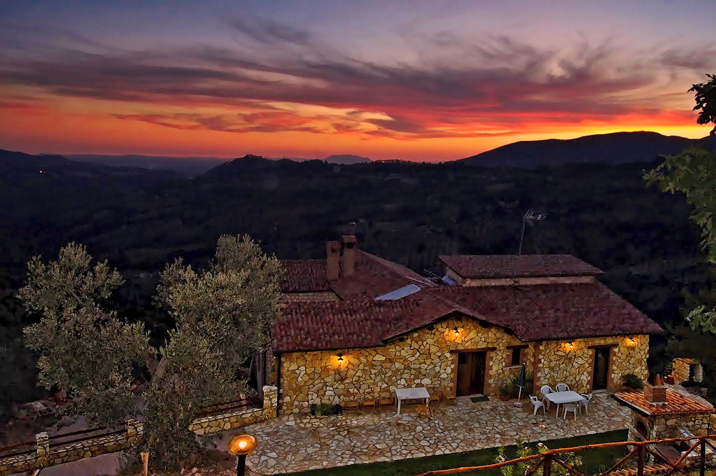 A stone house with a tiled roof, outdoor seating, and a view of the surrounding hills.