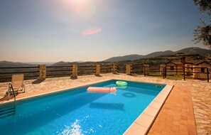 A swimming pool with a stone deck, a stone fence, and a view of distant hills. - Villa Elsa, with a pool and breathtaking views of the Roman countryside (Lazio)