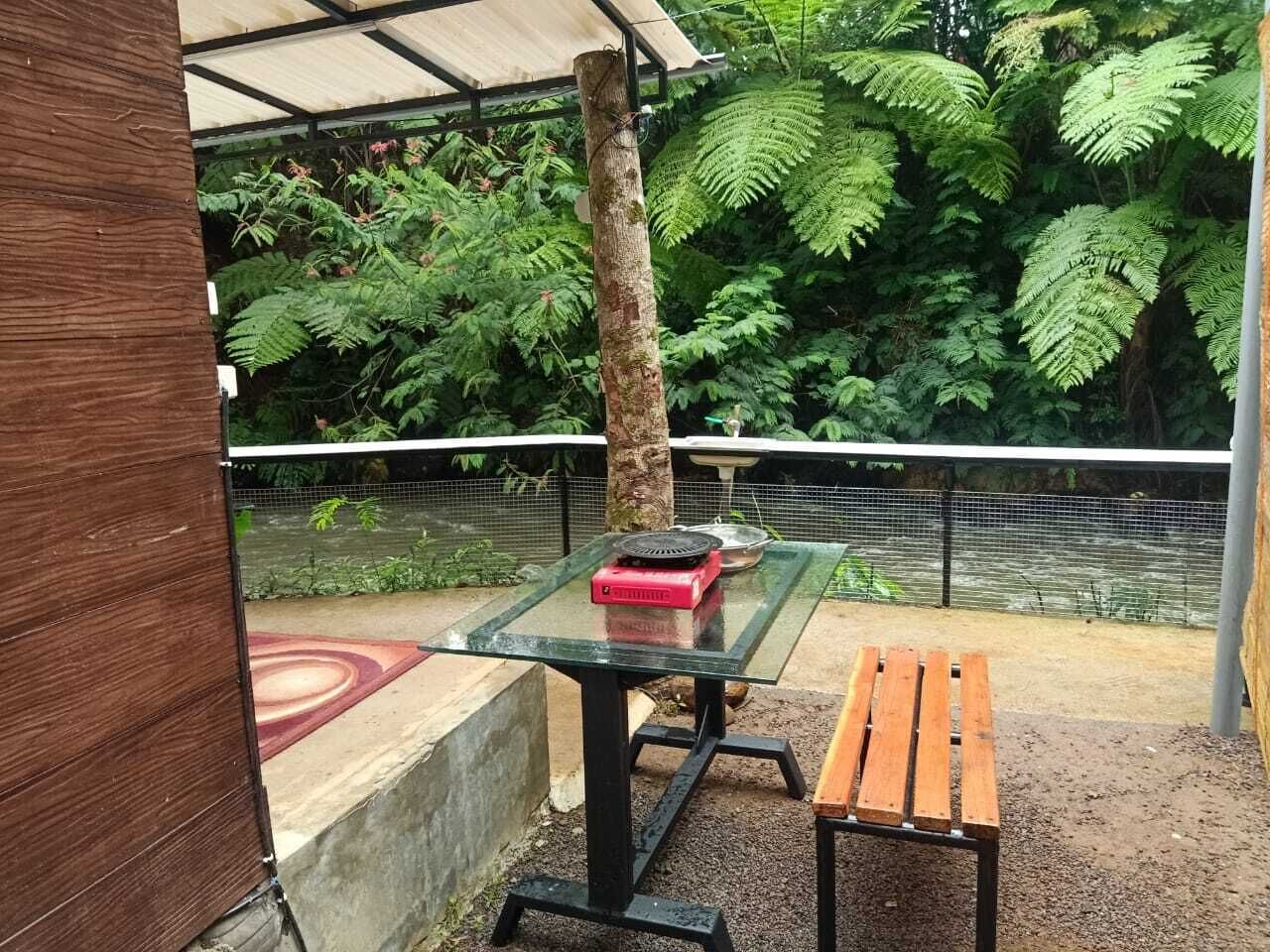 Un espace extérieur aménagé avec une table en verre, un objet rouge posé dessus et un banc en bois.