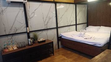 A hotel room with a bed, a wooden bedside table with amenities, a marble-patterned wall, and a ceiling-mounted air conditioning unit.