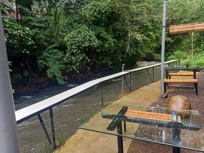 A riverside walkway with a metal railing, benches, and a wooden structure. - Cozzy Haruman riverside camp (Pangalengan)
