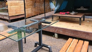 Un'area campeggio completa di un'area pranzo coperta, un tavolo in vetro, panche di legno e una tenda.