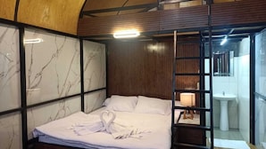 Una camera d'hotel con un letto, un comodino con una lampada, un soffitto in legno e vista sul bagno.