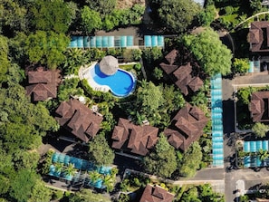 An aerial view of a resort with multiple bungalow-style buildings, a central swimming pool, and surrounding greenery. - Luxury 2bed 2bath poolside condo near beach (Villareal)