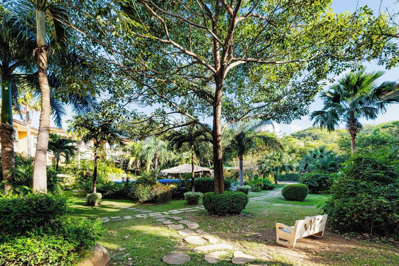A garden with a stone pathway, a bench, and a thatched-roof structure.
