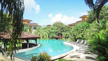 A swimming pool with a curved design, surrounded by lush greenery and palm trees.