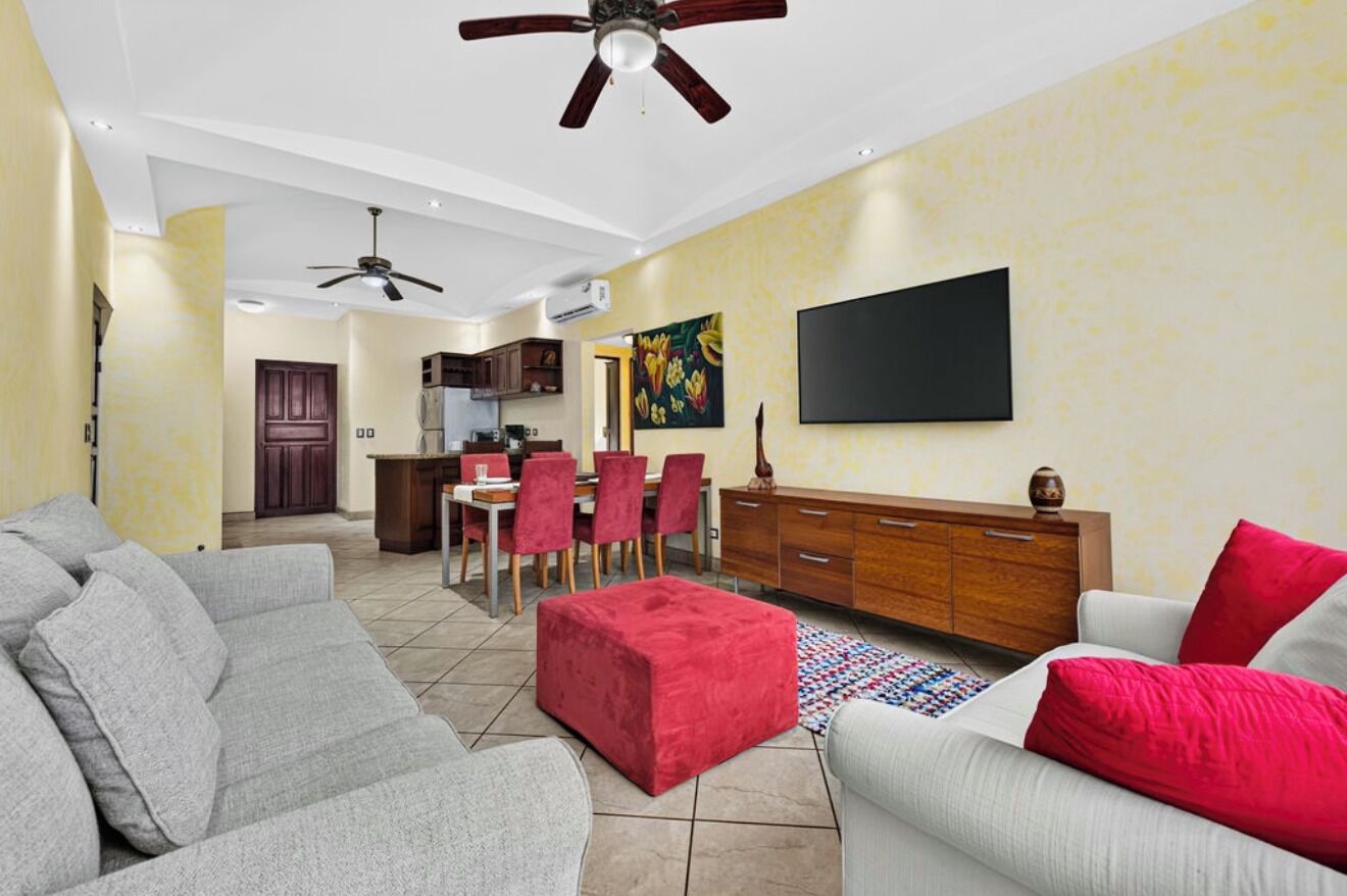 A living room with a sofa, ottoman, and a television mounted on the wall.
